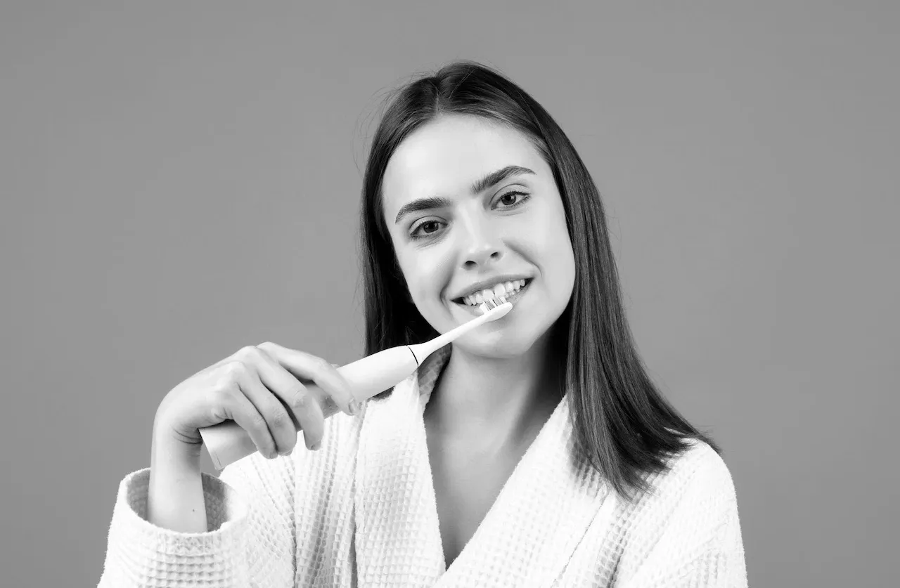 Persona cepillándose los dientes con un cepillo de cerdas suaves frente al espejo en una clínica dental moderna. Persona cepillándose los dientes con un cepillo de cerdas suaves frente al espejo en una clínica dental moderna.